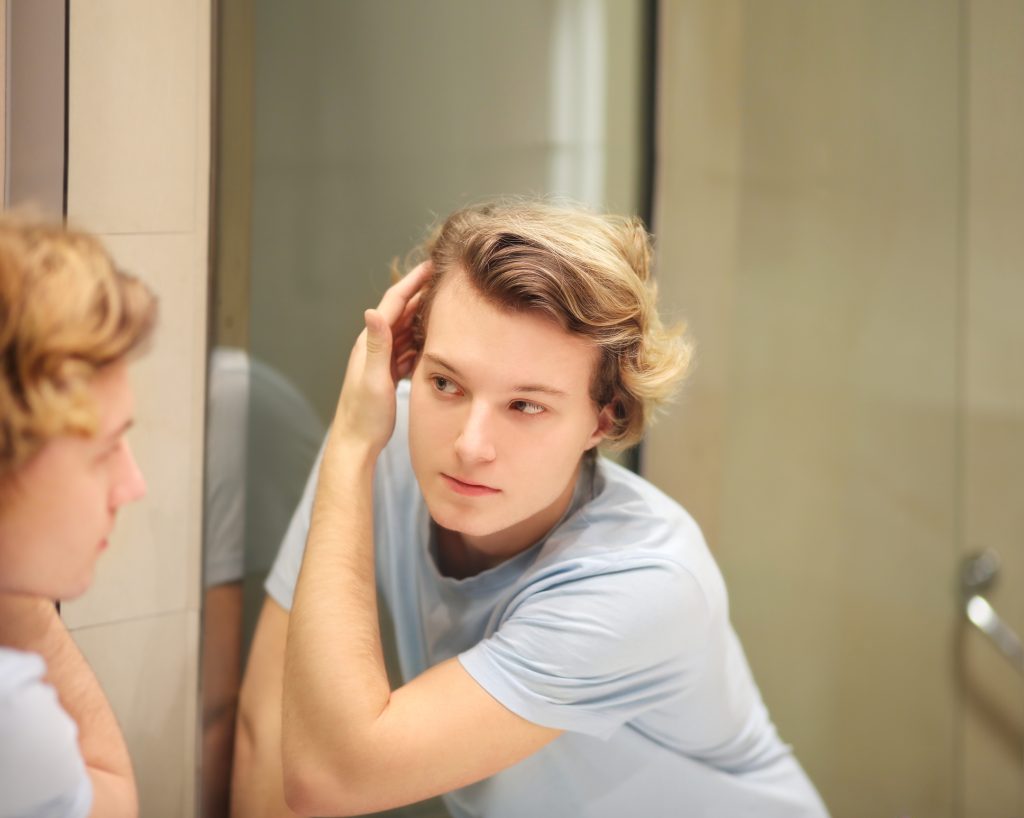 Teenager Looking In The Mirror And Combing His Hair